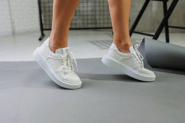 Genç, deri ayakkabılı, beyaz arka planda duran güzel bir kadın. Şık ayakkabılı kadın bacakları. Sıradan beyaz kadın ayakkabıları.