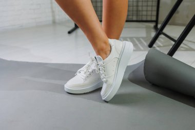 Genç, deri ayakkabılı, beyaz arka planda duran güzel bir kadın. Şık ayakkabılı kadın bacakları. Sıradan beyaz kadın ayakkabıları.