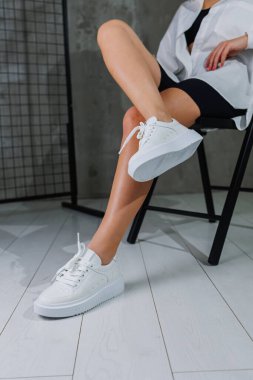 Deri beyaz spor ayakkabılarla güzel kadın bacakları. Şık ayakkabılı kadın bacakları. Sıradan beyaz kadın ayakkabıları.