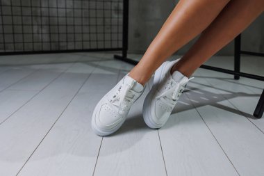 Deri beyaz spor ayakkabılarla güzel kadın bacakları. Şık ayakkabılı kadın bacakları. Sıradan beyaz kadın ayakkabıları.