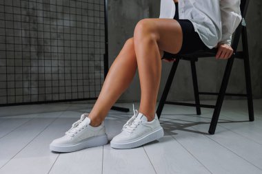 Deri beyaz spor ayakkabılarla güzel kadın bacakları. Şık ayakkabılı kadın bacakları. Sıradan beyaz kadın ayakkabıları.