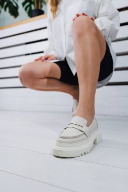 Beyaz deri ayakkabılar içindeki güzel kadın bacakları. Yaz kadın ayakkabıları.