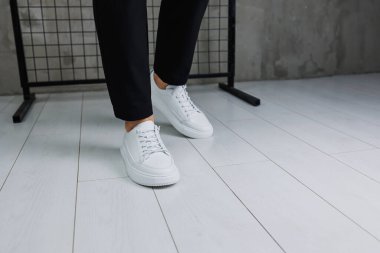 Siyah pantolonlu ve beyaz, klasik spor ayakkabılı erkek bacaklarına yakın çekim. Erkekler için deri ayakkabılar.