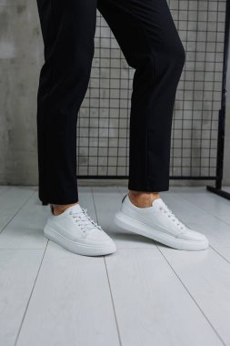 Siyah pantolonlu ve beyaz, klasik spor ayakkabılı erkek bacaklarına yakın çekim. Erkekler için deri ayakkabılar.