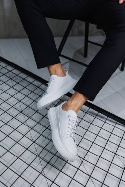 Siyah pantolonlu ve beyaz, klasik spor ayakkabılı erkek bacaklarına yakın çekim. Erkekler için deri ayakkabılar.