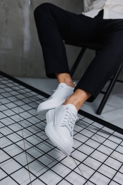 Siyah pantolonlu ve beyaz, klasik spor ayakkabılı erkek bacaklarına yakın çekim. Erkekler için deri ayakkabılar.