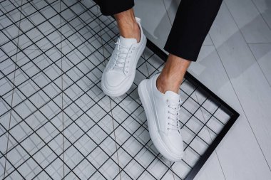 Erkek bacakları yakın plan. Şık siyah pantolonlu ve beyaz deri ayakkabılı bir adam. Günlük bakışın ayrıntıları. Erkekler sokak modası