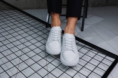 Erkek bacakları yakın plan. Şık siyah pantolonlu ve beyaz deri ayakkabılı bir adam. Günlük bakışın ayrıntıları. Erkekler sokak modası