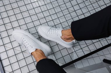 Erkek bacakları yakın plan. Şık siyah pantolonlu ve beyaz deri ayakkabılı bir adam. Günlük bakışın ayrıntıları. Erkekler sokak modası