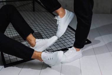 Siyah pantolonlu ve beyaz spor ayakkabılı kadın ve erkek bacaklarına yakın çekim. Yaz erkek ve kadın deri ayakkabıları