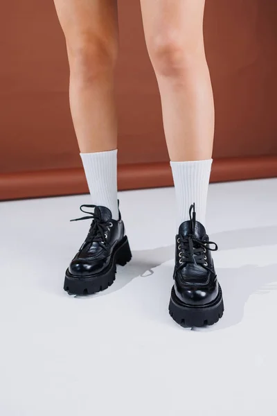 Beautiful female legs in black leather lace-up loafers. Female legs with fashionable shoes and white socks. Casual black women's shoes