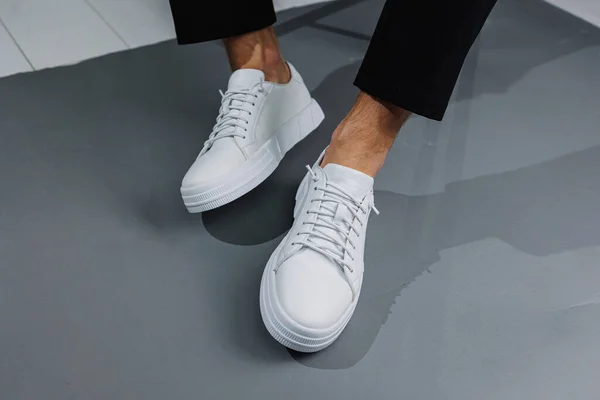 Modern men's shoes. Male legs in black pants and white casual sneakers. Men's fashionable shoes