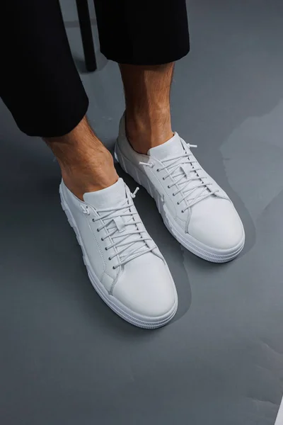 Modern men's shoes. Male legs in black pants and white casual sneakers. Men's fashionable shoes