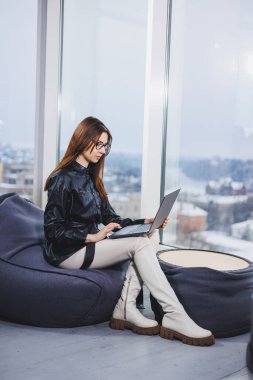 Gözlüklü genç ve güzel bir kadın modern bir çalışma alanında otururken dizüstü bilgisayarda çalışıyor. Uzak çalışma, serbest çalışma