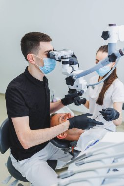 Hastaları tedavi etmek için mikroskobu olan modern bir diş kliniği. Bir dişçi hastanın dişlerini incelemek için mikroskop kullanır. Tıbbi ekipman, diş sağlığı kliniği.