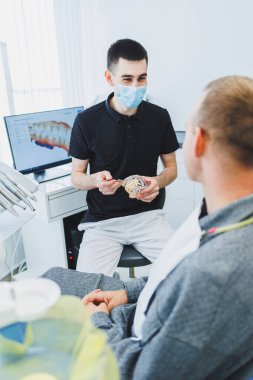 Modern bir diş muayenehanesindeki bir diş hekimi hastasına diş bakımından bahseder. Bir adam dişçi koltuğunda oturur ve dişçiyi dinler..