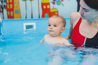 Bir yüzme öğretmeni küçük bir çocuğa havuzda yüzmeyi öğretir. Çocukların ilk yüzme dersleri. Bebekler için geliştirme