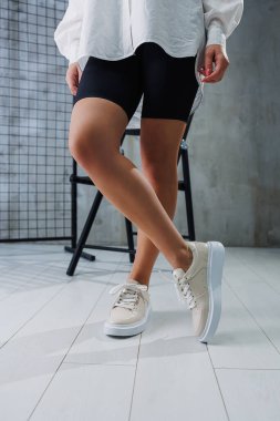 Female slender legs in beige casual sneakers with laces. Women's stylish leather summer shoes