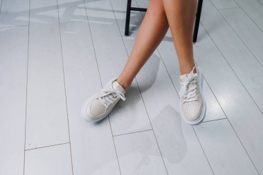 Female slender legs in beige casual sneakers with laces. Women's stylish leather summer shoes