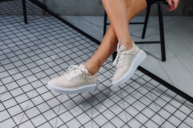 Female beautiful legs in beige casual sneakers. Women's stylish leather summer shoes