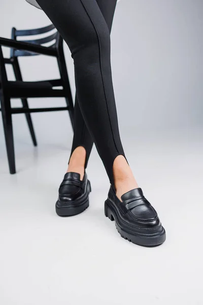 Women shoes. Close-up of female legs in black leggings and black leather loafers. New spring-summer collection of women\'s leather shoes