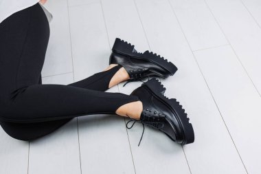 Close-up of black leather lace-up shoes on female legs in black leggings. Women's stylish autumn shoes