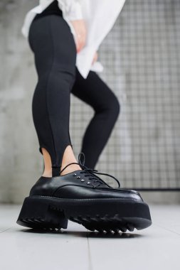 Close-up of black leather lace-up shoes on female legs in black leggings. Women's stylish autumn shoes