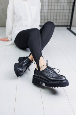 Close-up of black leather lace-up shoes on female legs in black leggings. Women's stylish autumn shoes