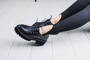 Close-up of black leather lace-up shoes on female legs in black leggings. Women's stylish autumn shoes