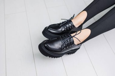 Close-up of black leather lace-up shoes on female legs in black leggings. Women's stylish autumn shoes