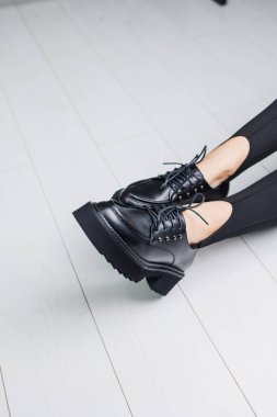 Close-up of black leather lace-up shoes on female legs in black leggings. Women's stylish autumn shoes