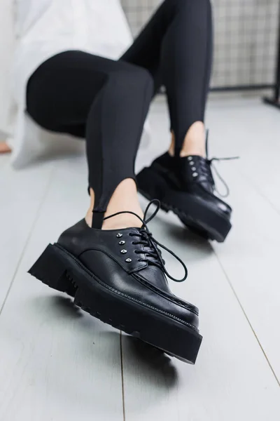 Close-up of black leather lace-up shoes on female legs in black leggings. Women's stylish autumn shoes