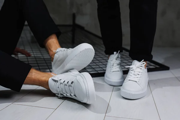 Summer shoes. Close-up of male and female legs in black pants and white casual sneakers. Summer leather shoes for men and women