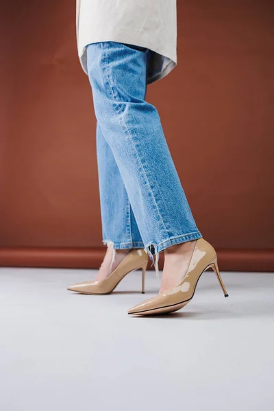 Close-up of female legs in blue jeans and fancy beige high heels. Women\'s leather pumps.