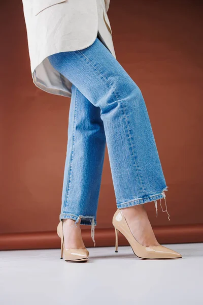 Close-up of female legs in blue jeans and fancy beige high heels. Women\'s leather pumps.