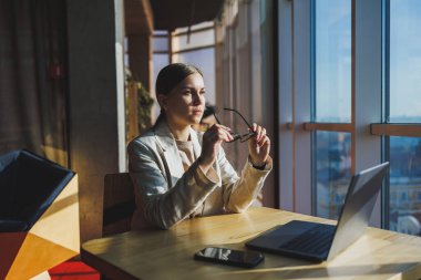Young content worker in casual clothes sitting at a desk and using a netbook while working on the background of a spacious office. Business woman in the office works sitting near the window