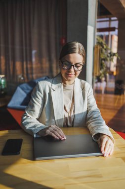 Young content worker in casual clothes sitting at a desk and using a netbook while working on the background of a spacious office. Business woman in the office works sitting near the window