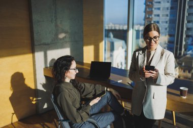 Smiling female colleagues collaborating indoors at table, woman wearing glasses and using laptop and showing partner. Business relations of serel colleagues in the office. Team work of colleagues