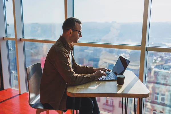 stock image A balanced man in glasses and casual clothes works on a laptop from a cozy workspace. A successful freelancer works remotely.