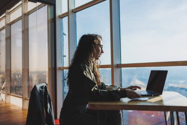 Young freelancer woman. Young woman working with laptop in coworking space and talking on phone, sitting in open space with cup of coffee and smiling while holding glasses.