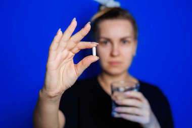 Smiling young woman without makeup in black t-shirt drinking vitamins for health, mature woman, natural beauty concept. Morning glass of water, immune care, vitamin complex for women. Selective focus
