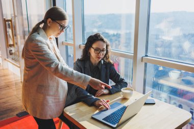 Two business women are looking for something in a laptop. Concept of business cooperation and teamwork. Young smiling women at the desk in the office. Modern successful people