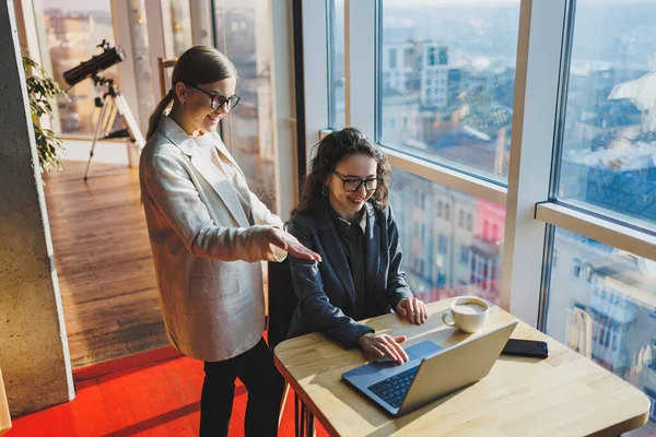 Two business women are looking for something in a laptop. Concept of business cooperation and teamwork. Young smiling women at the desk in the office. Modern successful people