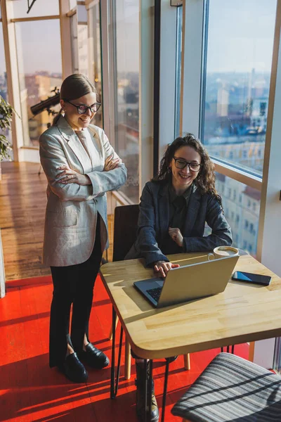 Two business women are looking for something in a laptop. Concept of business cooperation and teamwork. Young smiling women at the desk in the office. Modern successful people
