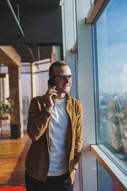 Modern office worker using smartphone app for service consultation in modern workspace, man talking on the phone. Remote work, male freelancer