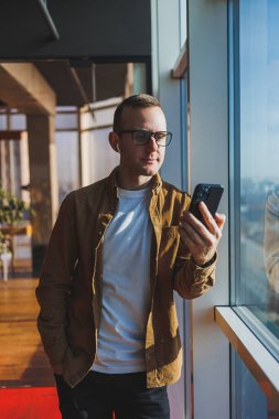 Modern office worker using smartphone app for service consultation in modern workspace, man talking on the phone. Remote work, male freelancer