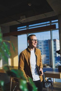 Young smart freelancer in casual clothes and glasses working on tablet working with documents and laptop computer at table. A student studying online with a netbook