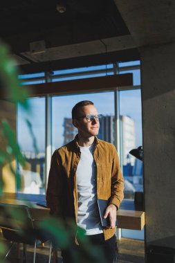 Young smart freelancer in casual clothes and glasses working on tablet working with documents and laptop computer at table. A student studying online with a netbook