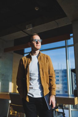 Young smart freelancer in casual clothes and glasses working on tablet working with documents and laptop computer at table. A student studying online with a netbook