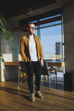 Young smart freelancer in casual clothes and glasses working on tablet working with documents and laptop computer at table. A student studying online with a netbook